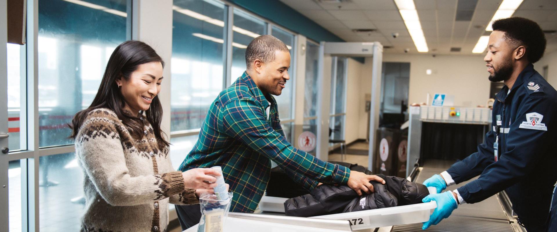 The image depicts a man and a woman standing at the airport screening area