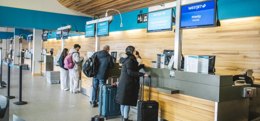The image depicts a busy airport scene with several people standing in line at a check-in counter.